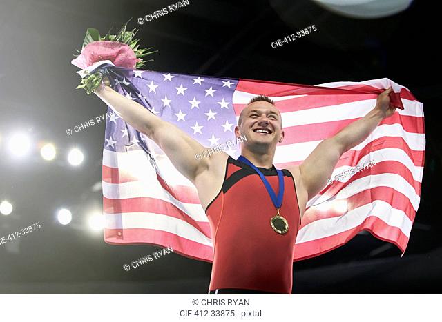 Enthusiastic male gymnast celebrating victory holding American flag on winners podium