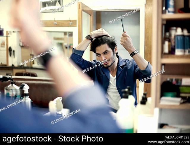Portrait of barber fixing hair in front of mirror in barber shop