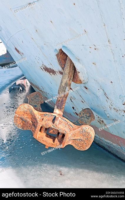 Old rusty anchor on the bow of the ship frozen into the ice. Close-up
