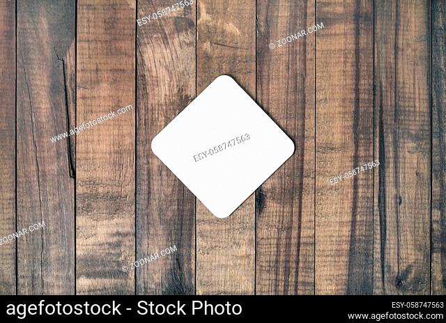 Blank square beer coaster on wood table background. Responsive design mockup. Flat lay