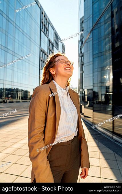 Smiling businesswoman with eyes closed standing on footpath