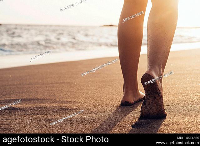 Beach travel - woman walking on sand beach leaving footprints in the sand. Closeup detail of female feet and golden sand on Tenerife beach