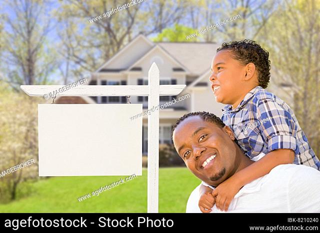 Happy african american father and mixed-race son in front of blank real estate sign and new house