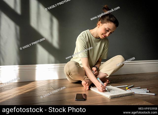 Smiling woman drawing on note pad while sitting on floor