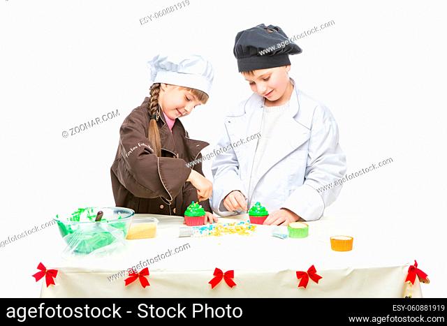 Beautiful boy and girl in chef clothes making christmas cupcakes. Children standing isolated over white background