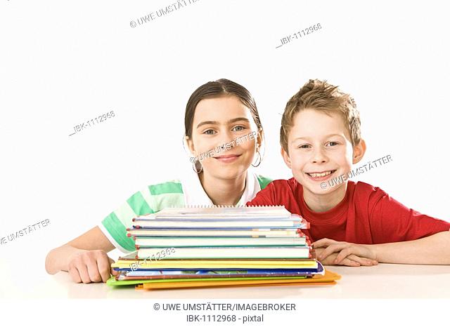 Smiling girl and boy sitting in front of a pile of exercise books and school books