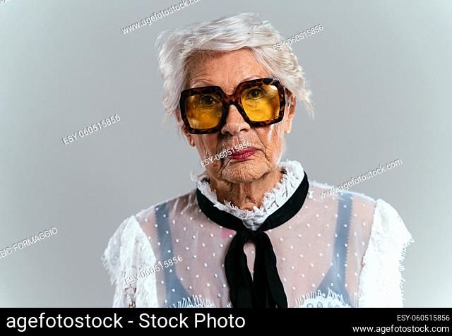 beautiful and elegant old influencer woman. Cool grandmother posing in studio wearing fashionable clothes. Happy senior lady celebrating and making party