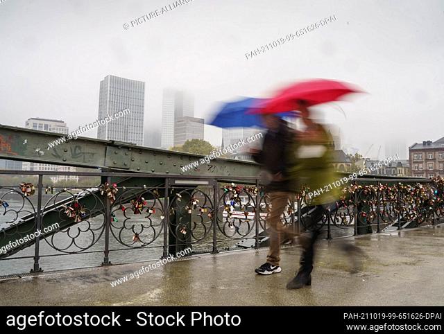 19 October 2021, Hessen, Frankfurt/Main: Two passers-by walk in grey rainy weather over the Eiserner Steg, a pedestrian bridge over the Main