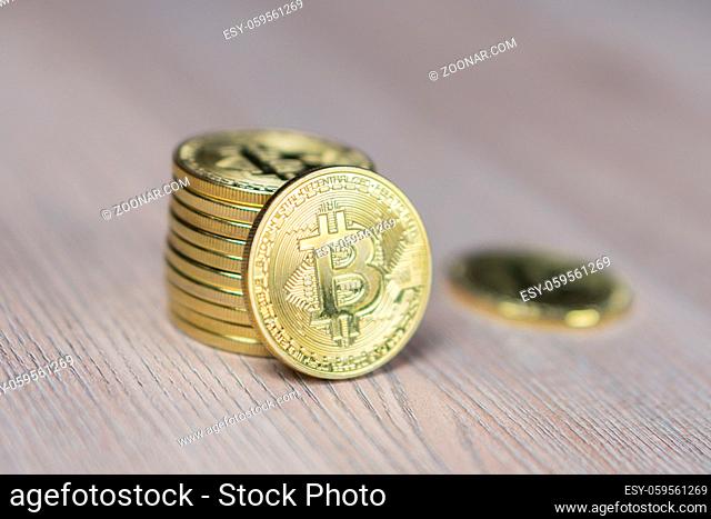 Stack of bitcoins with gold background with a single coin facing the camera in sharp focus with shading on the icon letter B on the face of the bit coin