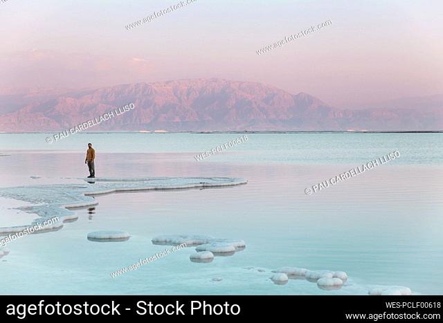 Man standing on salt formations in front of mountain at sunset