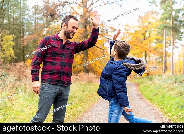Smiling man giving high-five to boy while standing at forest
