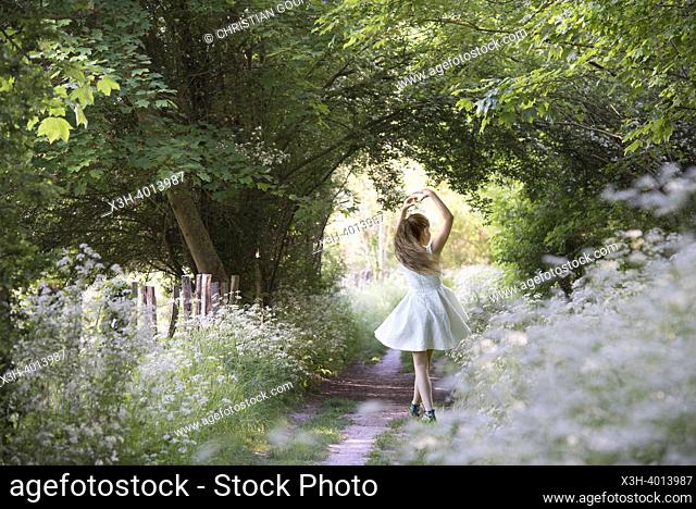 Girl performing a position (5th) of classical dance on a small country trail bordered by umbellifers on the edge of the forest, Eure-et-Loir department