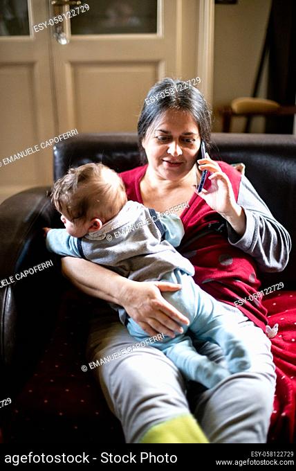 mother with little son in her arms, talking on smartphone sitting on the sofa