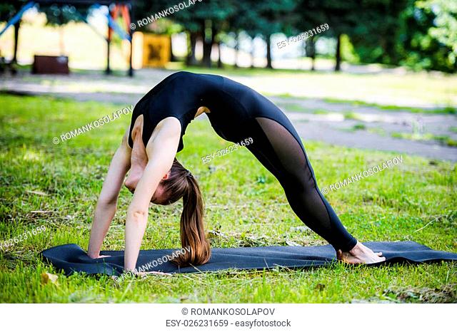 Fit young beautiful woman wearing black sporty leggings working out outdoors in park on summer day, doing Bridge Pose, Urdhva Dhanurasana Upward Bow