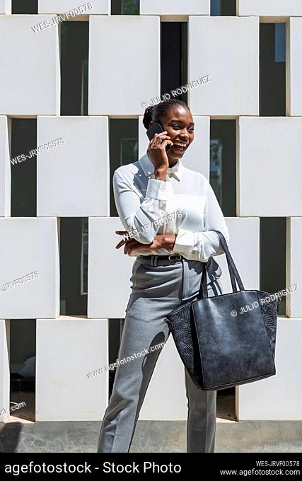Cheerful businesswoman talking on mobile phone in front of wall