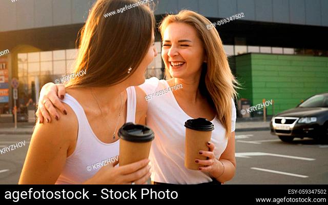 Happy smiling girls drinking coffee while walking on shopping mall car parking