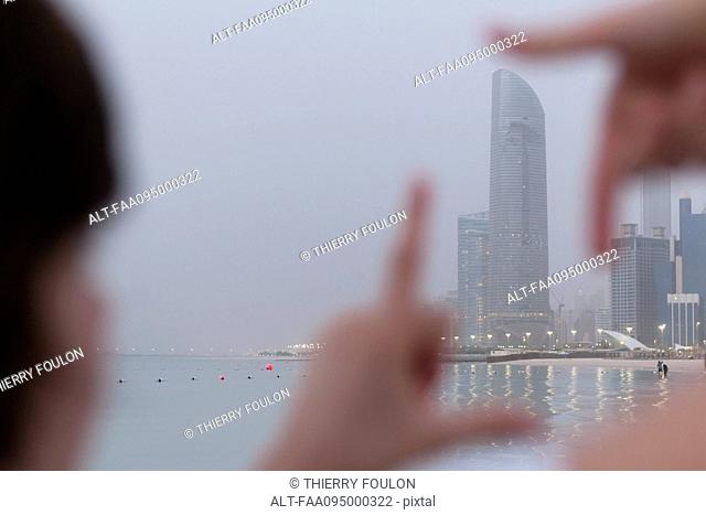 Person looking through finger frame at coastal skyscraper