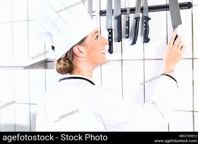 Female chef in uniform in industrial kitchen taking knife from wall bracket