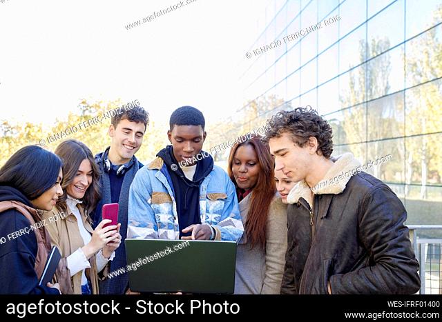 Teenage boy pointing at laptop with friends on college campus