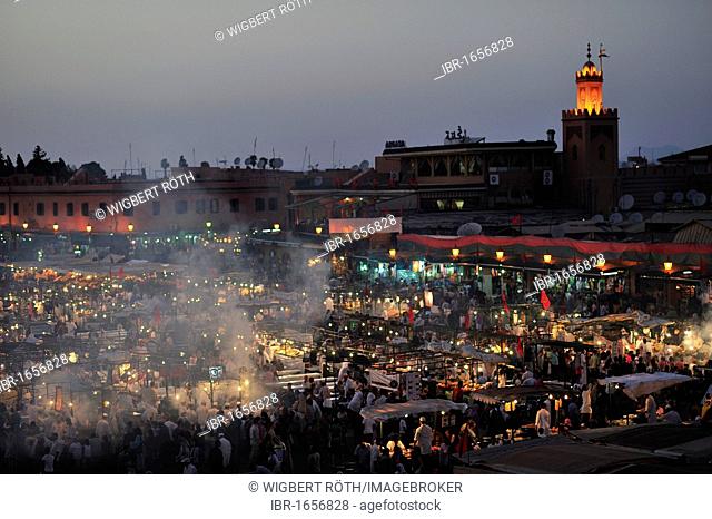 Evening at the Djemaa el Fna market square, literally meaning Assembly of the Dead, with smoke from the many food stalls, behind, the minaret of a mosque