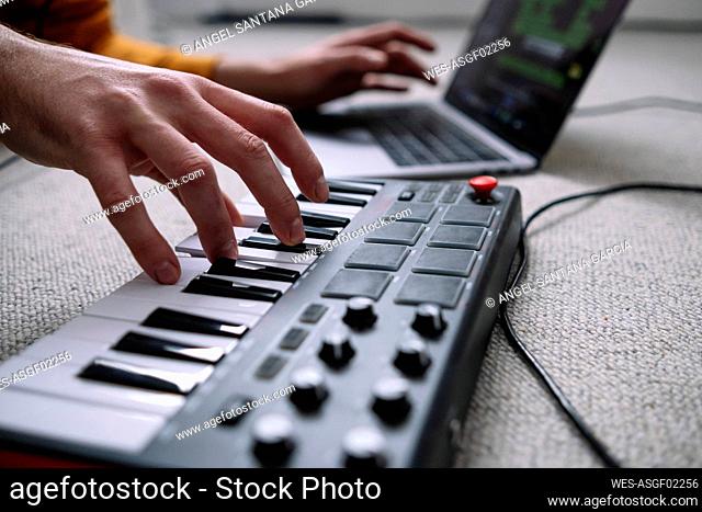 Hands of freelancer using laptop and piano in home studio