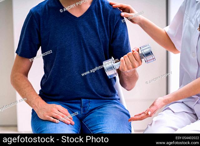 Therapist Assisting Male Patient While Exercising With Dumbbell