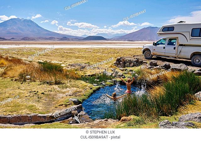 Two boys playing in water pool beside parked recreational vehicle, Salar de Chiguana, Chiguana, Potosi, Bolivia, South America