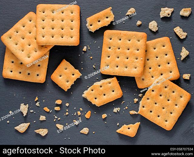 Square crackers with pieces and crumbs on slate gray background. Dry salt cracker cookies with fiber and dry spices. Top view or flat lay