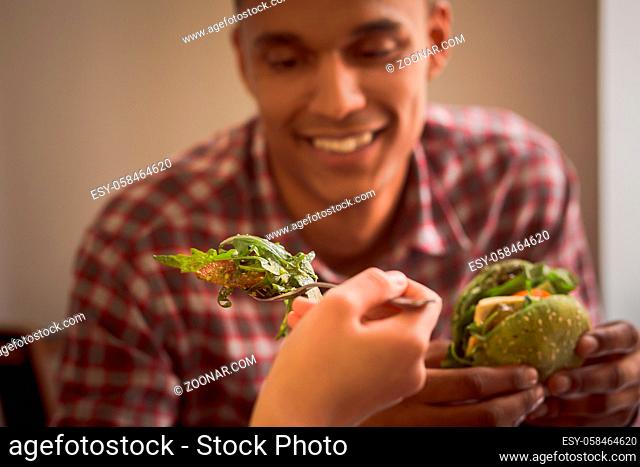 Closeup picture of lady feeding her boy-friend with vegan salad. Happy couple spending free time in vegan restaurant or cafe