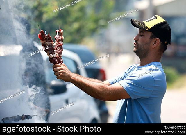 UZBEKISTAN, TASHKENT - JULY 9, 2023: A man cooks shashlik skewered meat during the 2023 early presidential election. The approved amendments to the Constitution...