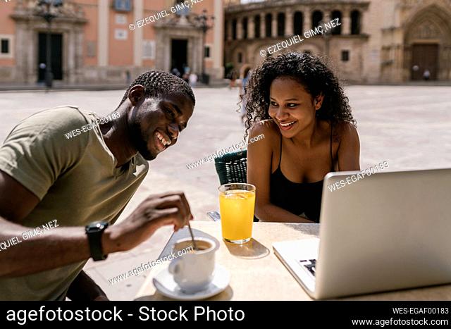 Happy couple using laptop at sidewalk cafe