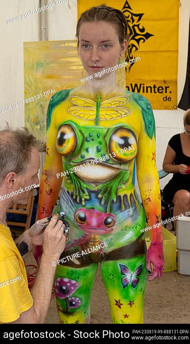 19 August 2023, Mecklenburg-Western Pomerania, Heringsdorf: Body painting artist Torsten Winter paints a model at the Bodypainting Festival in the seaside...