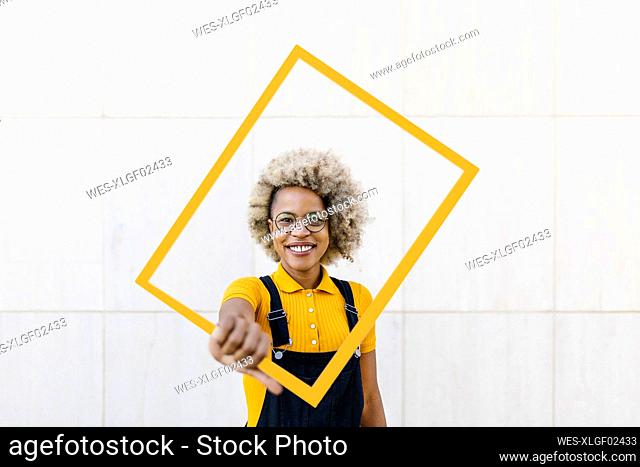 Woman holding yellow frame in front of wall