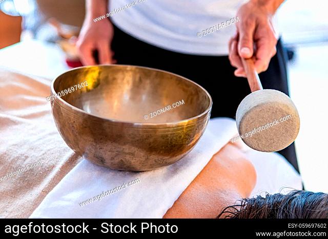 A masseur standing with a Tibetan bronze sound bowl with a stick. A professional massage therapist giving a sound massage