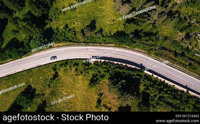 Aerial view of car on the move on road amidst lush green forest. Car passing on road through beautiful green forest cover
