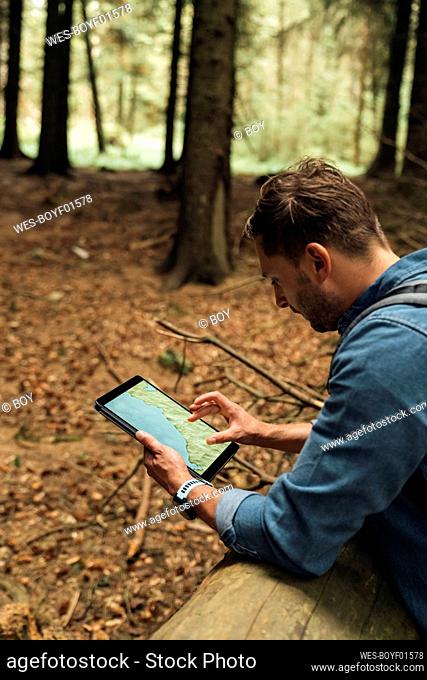 Male hiker analyzing map on digital tablet while standing in forest