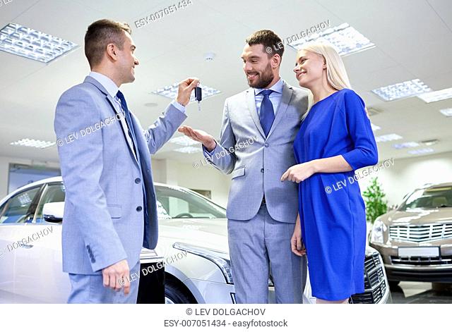 auto business, sale and people concept - happy couple with dealer giving car key in auto show or salon