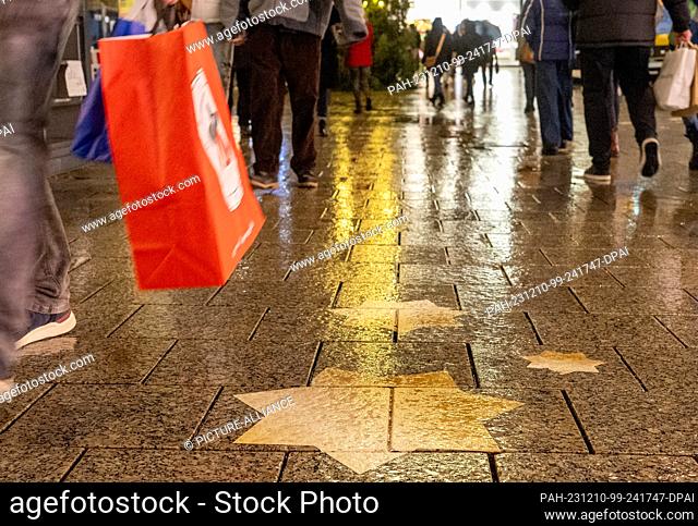 PRODUCTION - 09 December 2023, Baden-Württemberg, Ulm: In the city center, passers-by walk over wet pavement with bags while Christmas shopping