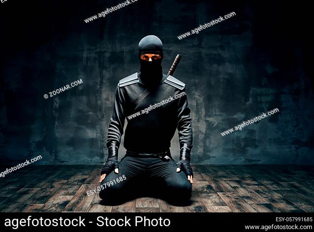 Ninja kneeling posing with a sword over black background. japanese fighter concept