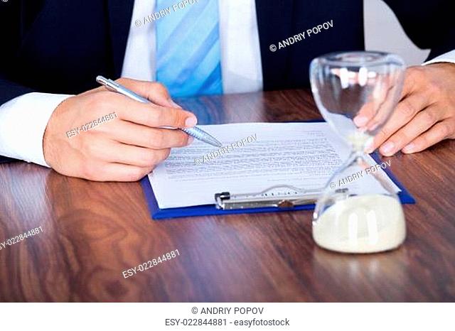 Businessman Filling Form In Front Of Hourglass