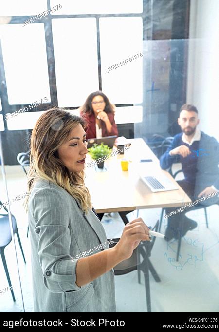 Businesswoman discussing business plan with male and female colleagues seen through glass at office