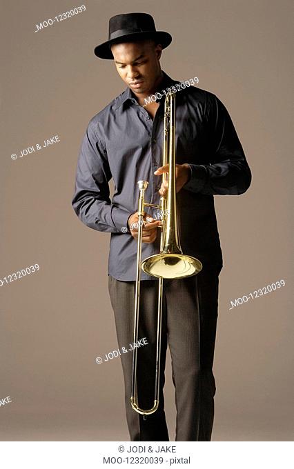 Trombonist standing wearing hat looking at trombone