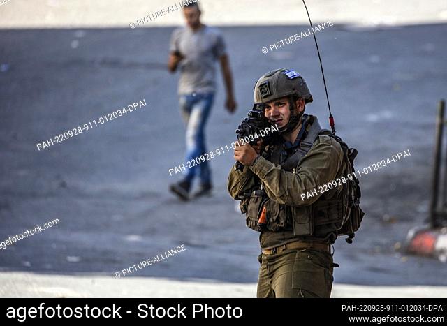 28 September 2022, Palestinian Territories, Hebron: An Israeli soldier aims his weapon during clashes with Palestinian protesters in the West Bank city of...