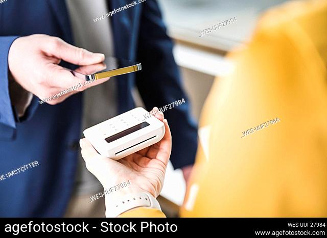 Young businessman paying through smart phone on card reader machine
