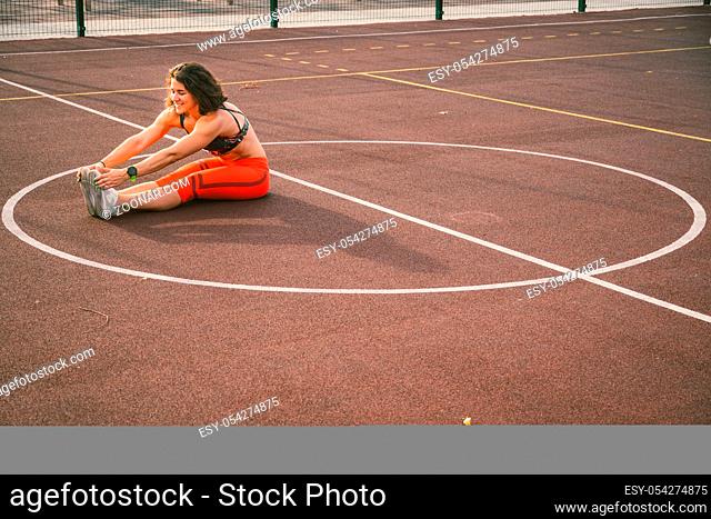 Woman Athlete Stretching Legs On Stadium. Female Runner Stretching Before Workout. Lifestyle portrait of athletic girl doing warm up and workout and stretching