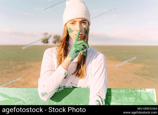 Young woman putting finger of green hand on her mouth