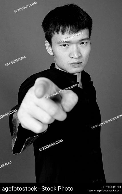 Studio shot of young Chinese man wearing traditional clothes against gray background in black and white