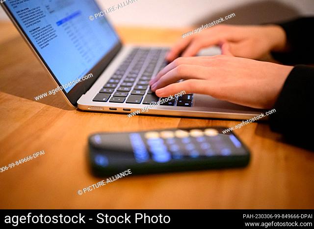 PRODUCTION - 12 February 2023, Hamburg: A woman sits at her laptop with calculator app on her phone (posed scene). Photo: Jonas Walzberg/dpa