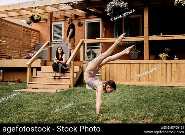 Girl doing acrobatics in garden, parents on terrace