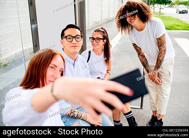 Mixed race group of friends hanging out together in town, taking selfie with mobile phone